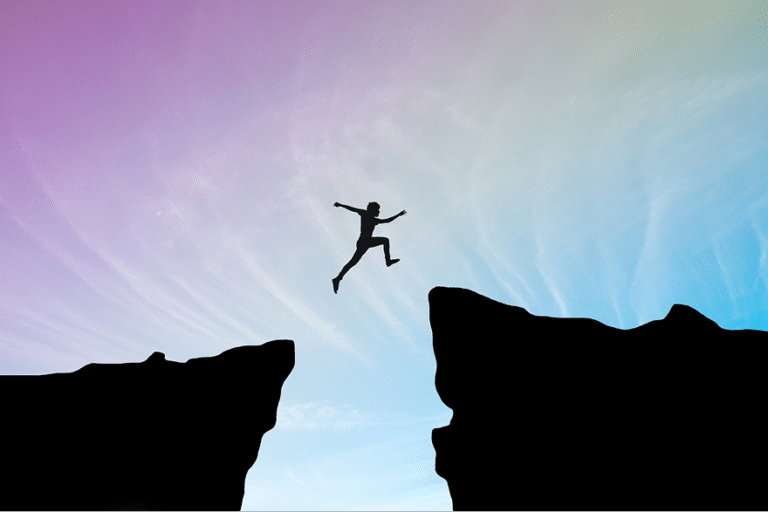Silhouette of a person mid-jump between two cliffs against a pastel gradient sky.