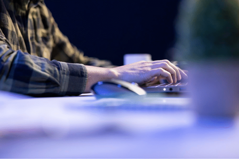Hands typing on a laptop keyboard on a desk, with a wireless mouse beside it.