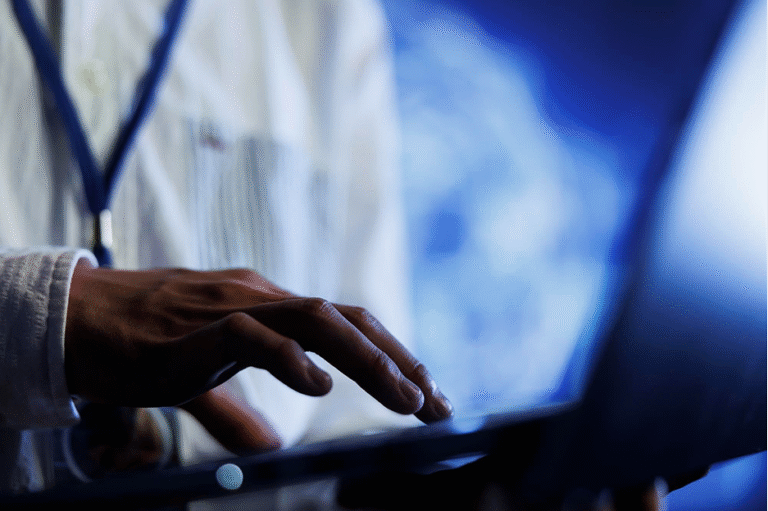 Medical professional typing on a tablet in a blue-lit clinical setting, hands in focus