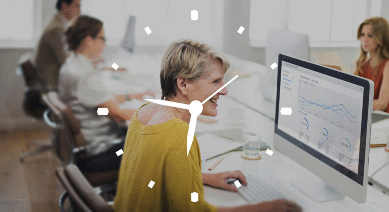 Smiling woman in a yellow top at a desktop computer, dashboards on screen; colleagues working in the background.